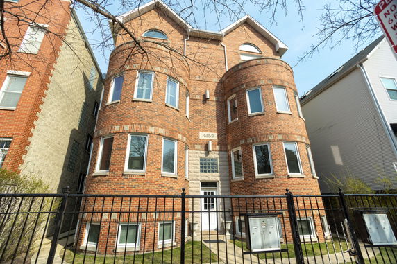 Front view of a multi-story brick building with rounded bay windows and a gated entrance.