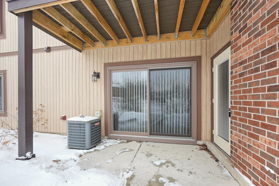 View of a house with a sliding glass door and brick exterior, featuring a small outdoor area and overhang.