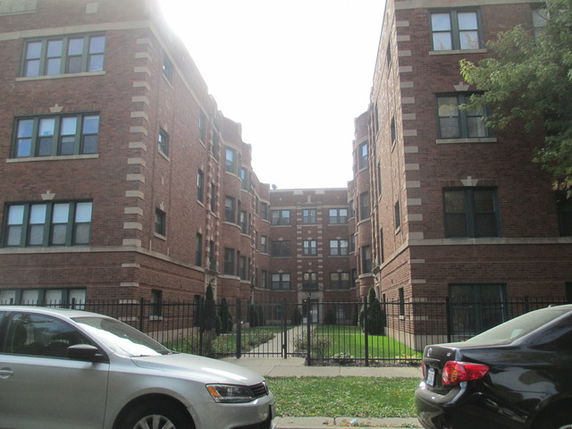 Front view of a multi-story brick apartment building with gated entry.