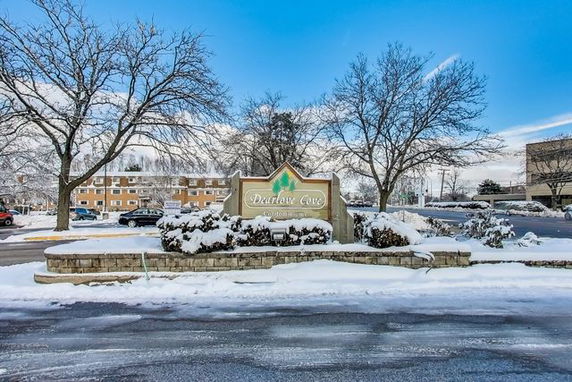 Front view of a snow-covered apartment building complex with a sign reading 'Darby Cove'.