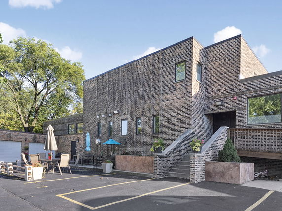 Front view of a modern two-story brick building with an outdoor seating area and stairs leading to an entrance.