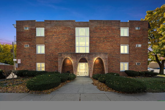 Front view of a brick apartment building with arched entryway and lit exterior.