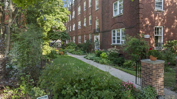 Front view of a brick building with multiple windows surrounded by greenery.