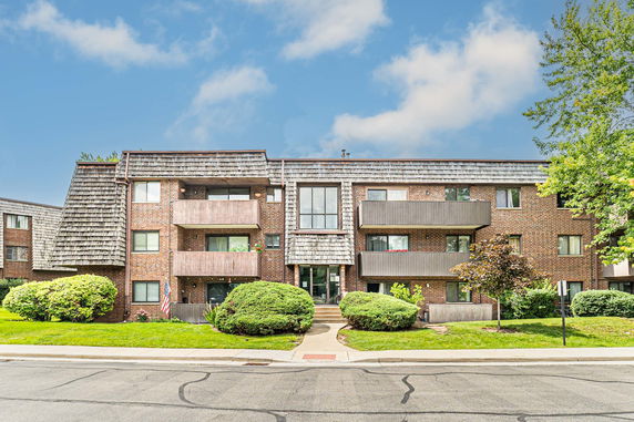 Front view of a multi-story brick building with balconies and a shingled roof.