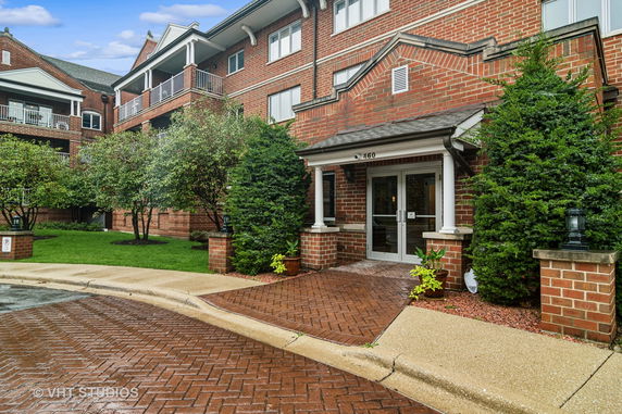 Front view of a multi-story brick building with balconies and a landscaped entrance.