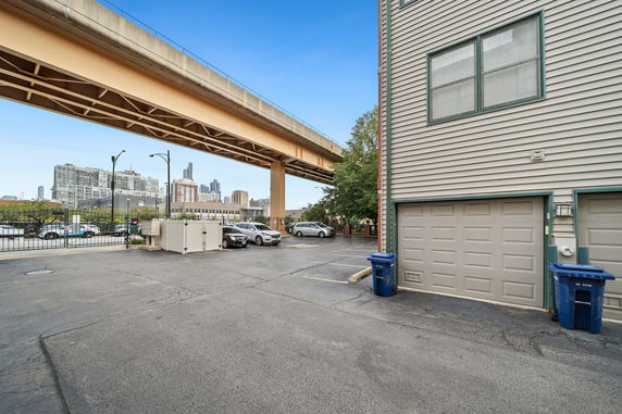 Outdoor parking area near a building with a garage and cars parked under an elevated railway.