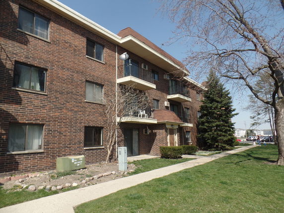 Front view of a three-story brick apartment building with balconies.