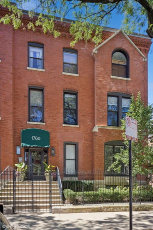 Front view of a three-story brick building with arched windows and an awning.