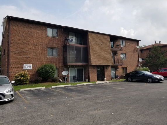 Front view of a three-story brick apartment building with balconies and parked cars.