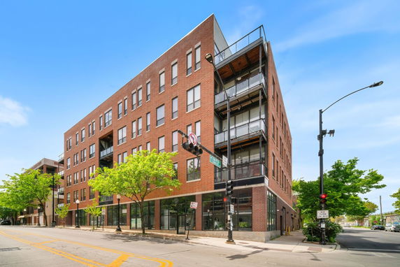 Front view of a multi-story brick building on a corner with glass balconies and large windows.
