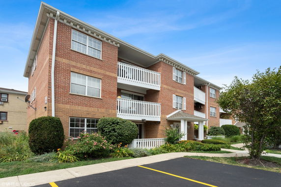 Front view of a three-story brick apartment building with white balconies.
