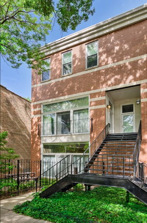 Front view of a brick multi-story building with stairs leading to the entrance.
