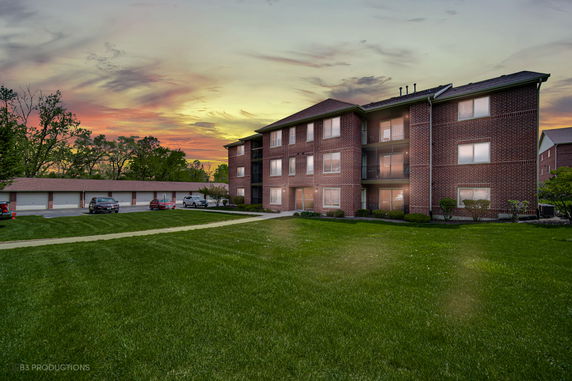 Front view of a three-story brick apartment building with garage units nearby.