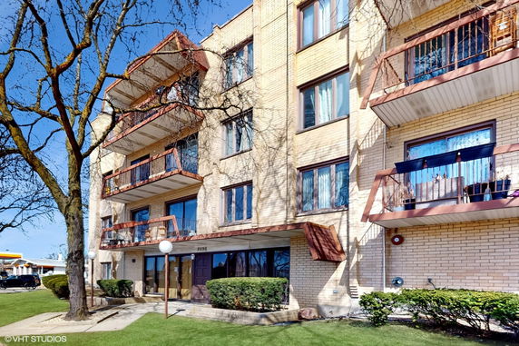 Front view of a multi-story apartment building with balconies and a tree in front.