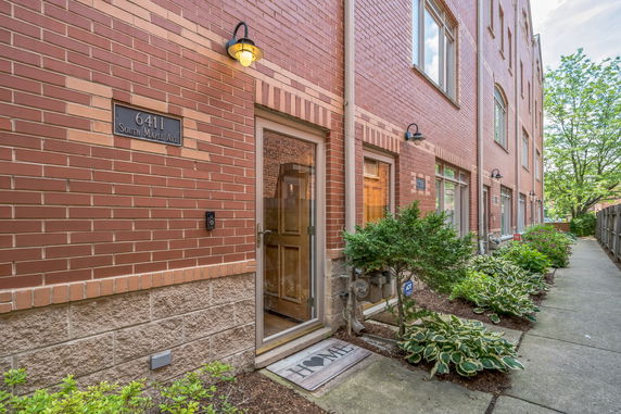 Front view of a brick townhouse entrance with a walkway and plants.
