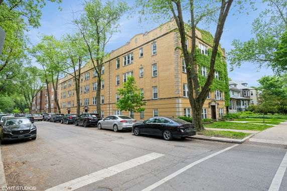 Street view of a four-story brick apartment building with greenery on the facade.