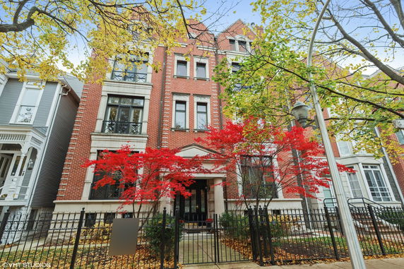 Front view of a multi-story red brick building with black framed windows and a gated entrance.