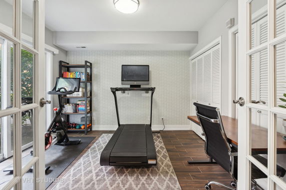 Indoor area featuring gym equipment including a treadmill and exercise bike, with shelves of books and a desk.