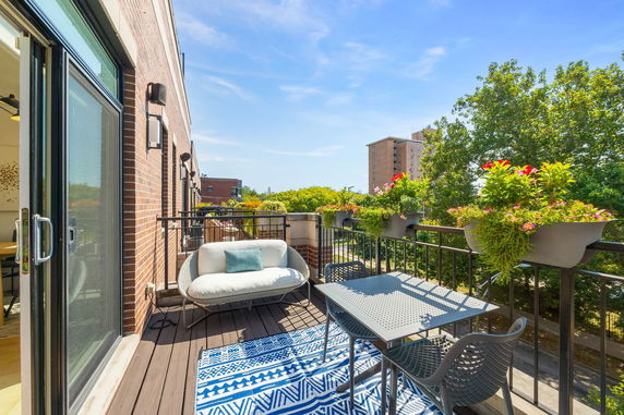 Balcony view with outdoor furniture and potted plants, facing surrounding buildings and trees.