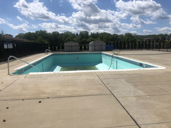 Outdoor swimming pool with surrounding pavement and fencing.