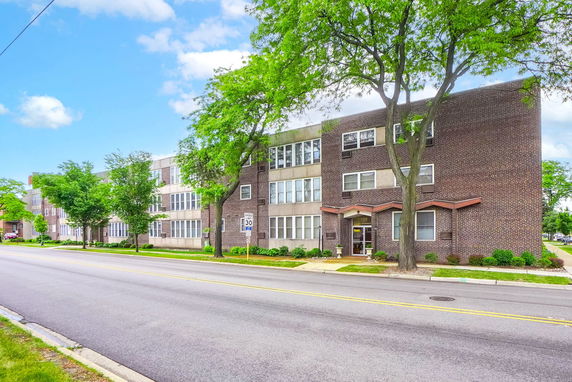 Front view of a three-story brick apartment building along a street with trees.