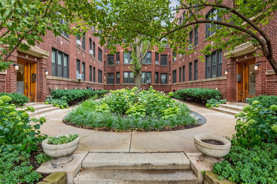 Front view of a brick apartment building with landscaped courtyard.