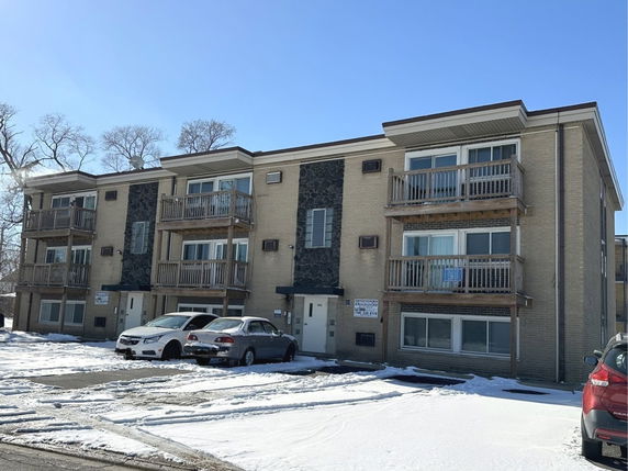 Front view of a three-story apartment building with balconies and parking area.
