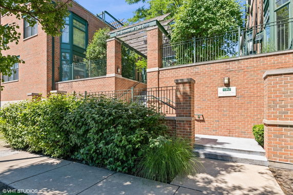 Front view of a brick building with a staircase and greenery.