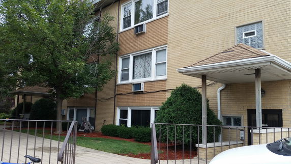 Front view of a multi-story brick building with windows and a small entrance with a canopy.