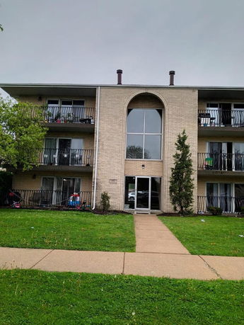 Front view of a three-story apartment building with balconies and a central glass entryway.