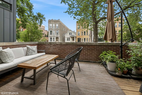 Balcony view with seating area overlooking surrounding buildings and trees.