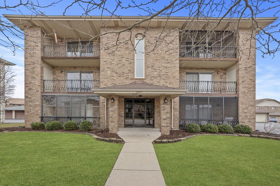 Front view of a three-story brick apartment building with balconies.