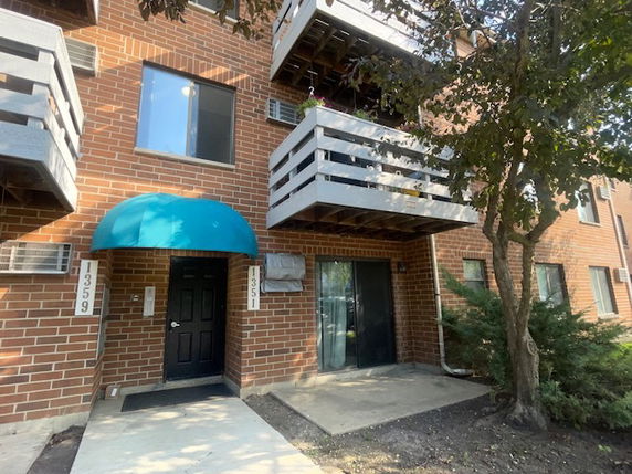 Front view of a multi-story brick building with balconies and a blue awning over the entrance.