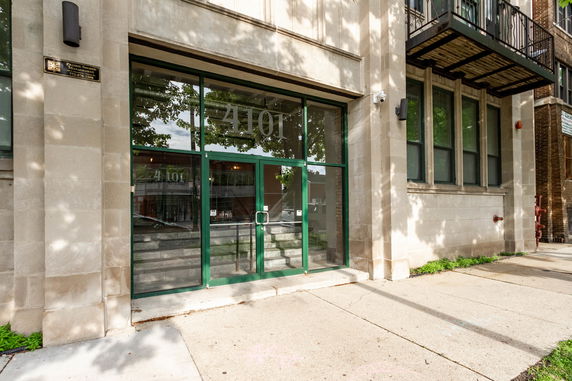 Front view of a building entrance with large glass doors and a balcony above.
