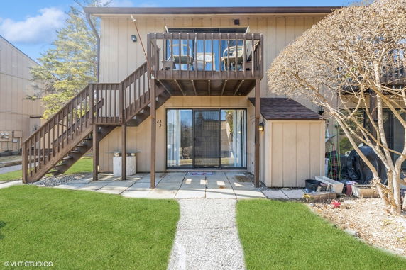 Back view of a two-story house with an upper deck and sliding glass doors on the lower level.