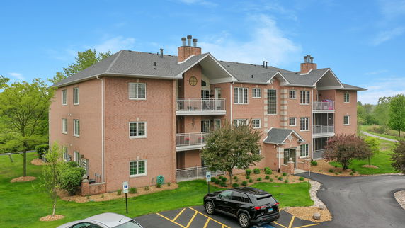 Front view of a multi-story brick apartment building with balconies and a parking area.