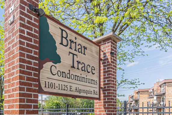 Front view of a condo complex with brick pillars and a wooden sign.
