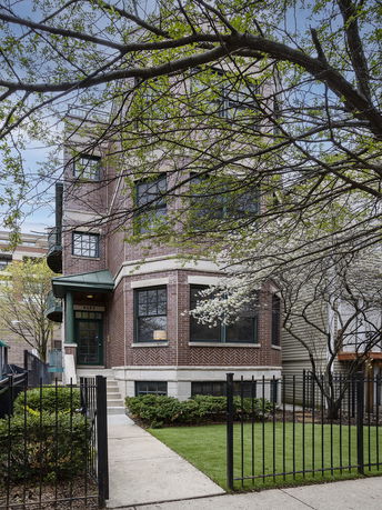 Front view of a multi-story brick house with a small front yard and black metal fence.