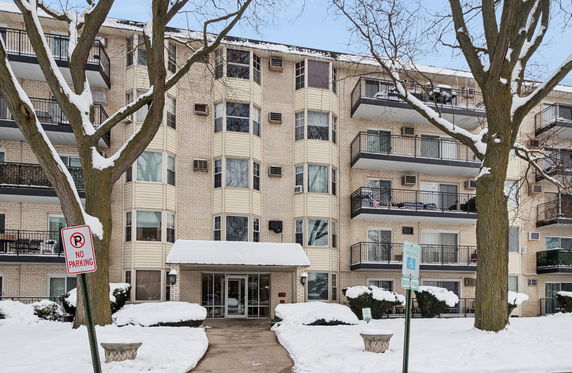 Front view of a multi-story residential building with balconies and snow-covered surroundings.