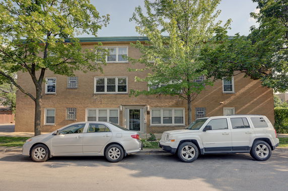 Front view of a three-story brick apartment building with parked cars.