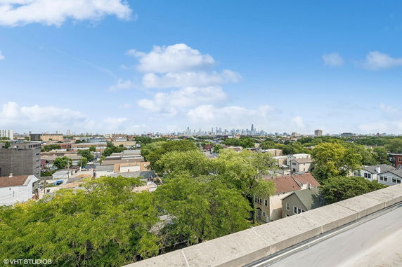 Panoramic view over a cityscape with buildings, trees, and a distant skyline.