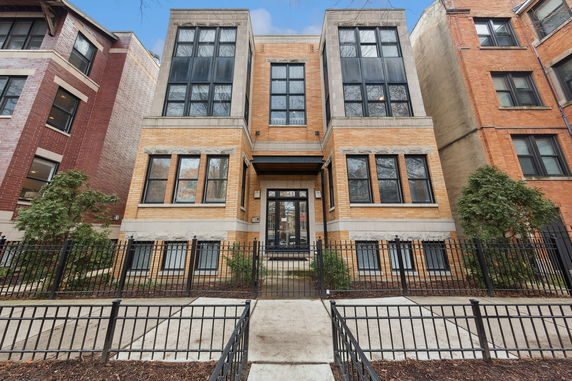 Front view of a multi-story brick building with large windows and iron fence.