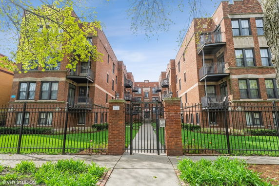 Front view of a multi-story brick apartment building with balconies and a gated entrance.