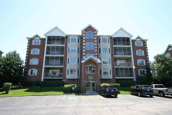 Front view of a multi-story building with a brick facade and parking area.