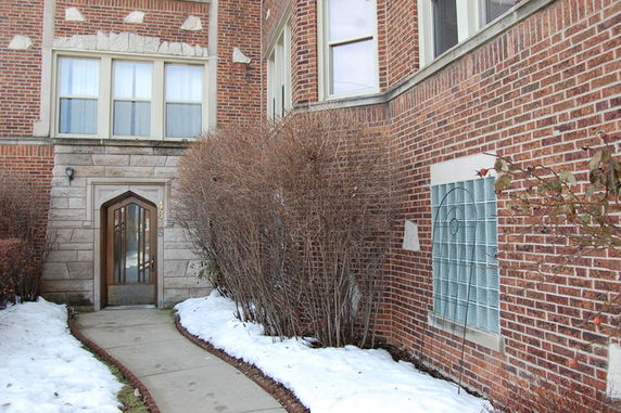Front view of a multi-story brick building with a distinctive entrance door and snow-covered path.