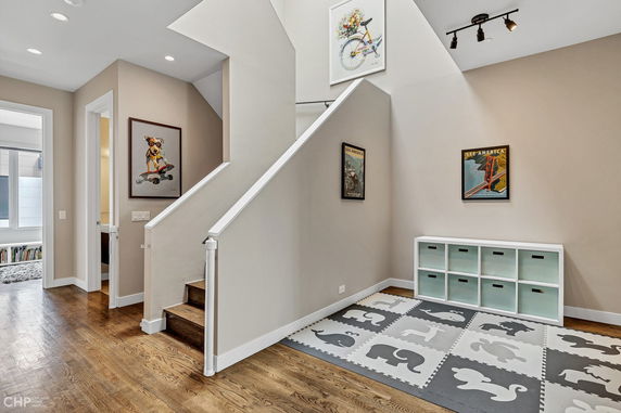 Interior view of a hallway with stairs, artwork on walls, and a play mat with storage bins.