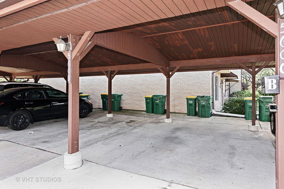 Covered parking area with cars and recycling bins.