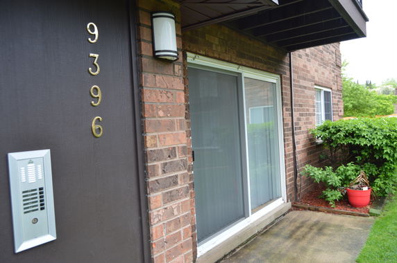Front view of a brick building with a sliding glass door and an intercom system.