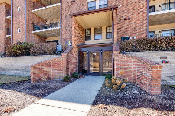 Front view of a brick apartment building entrance with stairs and a glass door.