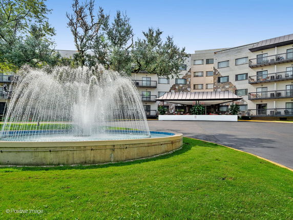 Front view of a multi-story building with balconies and a fountain.